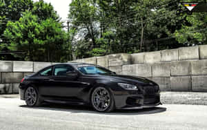 黑色BMW M6跑車停在混凝土牆和綠樹附近。 — Steam Deck OLED 壁紙