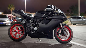 黑色Ducati電單車配紅色車輪，夜晚停在停車場。 — 機車 壁紙