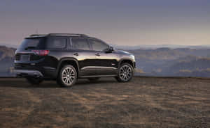 黑色GMC Acadia SUV停泊在俯瞰森林山脈的山丘上，夕陽西下。 — Steam Deck OLED 壁紙
