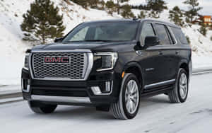 黑色GMC Denali SUV在積雪的山路上行駛，兩旁有常青樹。 — Steam Deck 壁紙