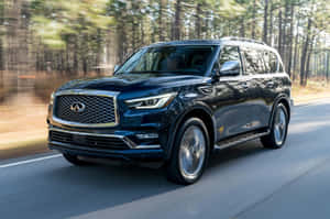 黑色Infiniti QX80 SUV在樹木成行的道路上快速行駛。 — Surface Laptop 壁紙