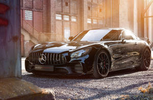 日落時分，黑色Mercedes-AMG GT停在碎石路上，前方是磚造建築。 — 平治 AMG 壁紙
