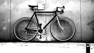 一輛黑色單車靠在一面有紋理的混凝土牆上，黑白畫面。 — 越野車 壁紙