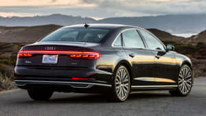 黑色奧迪A8 L轎車停在日落時分的沿海公路上，背景是山丘和海洋。 — Audi R8 GIF 壁紙