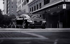 黑色奧迪雙門轎跑車停泊在城市街道上，背景有建築物和路牌。 — Audi R8 GIF 壁紙