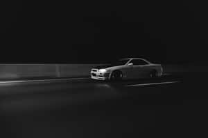 一輛銀色跑車在夜間獨自行駛在黑暗的高速公路上，車頭燈亮著。 — MacBook 壁紙