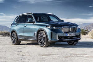 藍色BMW X5 SUV停在沙漠景觀中，背景有山脈。 — Surface Laptop 壁紙