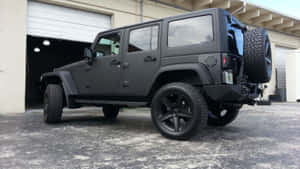 啞光黑色Jeep Wrangler停泊在混凝土場地上的車庫前。