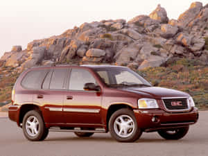 日落時分，栗色GMC Envoy SUV停泊在岩石沙漠山丘附近。 — 4:3 壁紙