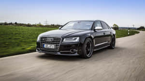 黑色 Audi 房車在鄉間道路上疾馳，有綠色田野和藍天。 — 奧迪 GIF 壁紙