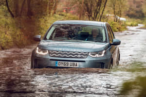 灰色 Land Rover Discovery 在潮濕道路上的泥濘森林水坑中行駛。 — MacBook Pro M4 壁紙