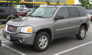 灰色GMC Envoy SUV停放在停車場，旁邊有其他汽車和一棟黃色建築物。 — 低飽和度 壁紙