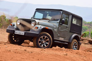 灰色Mahindra Thar SUV在靠近山丘的紅色泥路上行駛 — 汽車 壁紙