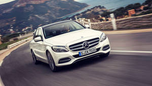 白色 Mercedes 房車在蜿蜒的沿海道路上快速行駛。 — 汽車 壁紙