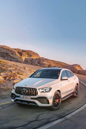 白色Mercedes-AMG GLE63 S Coupe在日落時分行駛在山路上。 — 2:3 壁紙
