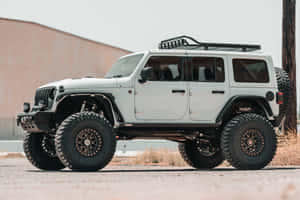 白色升高Jeep Wrangler停泊喺碎石上，有大輪胎同車頂行李架。 — Surface Laptop 壁紙