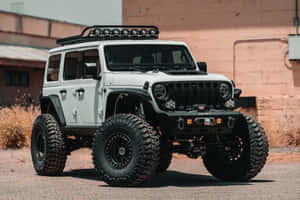 白色升高嘅Jeep Wrangler，配備大輪胎，停泊喺沙漠工業建築附近。 — MacBook Air M2 壁紙