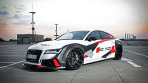 白色奧迪RS7，帶有紅黑賽車貼紙，停在日落時分的工業區停車場。