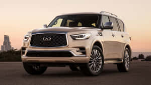 米色Infiniti QX80 SUV停泊在瀝青路上，背景有城市天際線和日落。 — 日落 壁紙