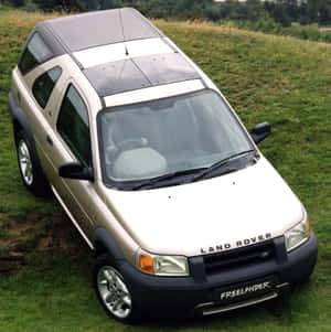 米色Land Rover Freelander SUV停泊在草木茂盛的山坡上。 — iPad 第9代 壁紙