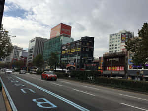 紅色SUV行駛在繁忙的城市街道上，有韓文招牌和現代建築。 — 日落大道 壁紙