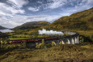 紅色蒸汽火車在蘇格蘭山區風景中穿越石拱橋 — MacBook Air M4 壁紙