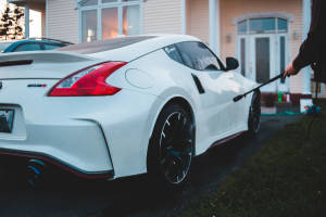 黃昏時分在屋前用水喉清洗白色日產370Z Nismo的人。 — 汽車 壁紙