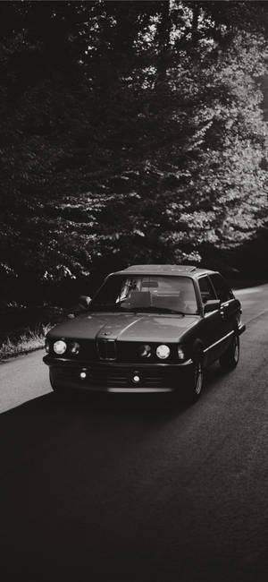 經典BMW E30房車在森林道路上以黑白行駛。 — Galaxy S25 FE 壁紙