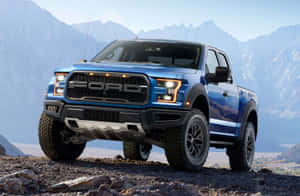 藍色福特 F-150 Raptor 卡車停在岩石地形上，背景有山脈。 — 老福特貨車 壁紙