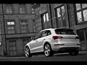 銀色 Audi Q5 SUV 停泊在磚建築旁的城市街道上。 — 奧迪 GIF 壁紙