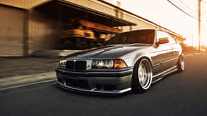 銀色BMW E36雙門轎跑車在金色日落時分於都市街道上疾馳。 — 酷車 壁紙