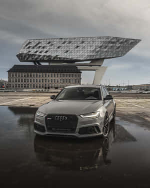 銀色奧迪 RS6 Avant 停在濕漉漉的瀝青路面上，背景有現代建築。 — Audi R8 GIF 壁紙