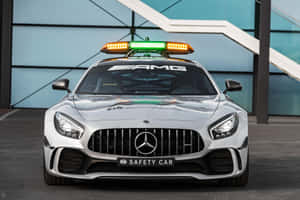銀色平治AMG F1安全車閃爍著警示燈，停在玻璃建築附近。 — Surface Pro 壁紙