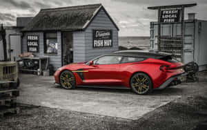 紅色Aston Martin Vanquish S停泊在海邊碎石停車場的魚棚附近。 — Steam Deck 壁紙