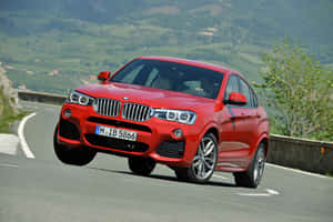 紅色BMW X4 SUV在蜿蜒的山路上行駛，周圍有綠色山丘。 — MacBook Air M2 壁紙