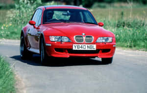 紅色BMW Z8在兩旁有綠化的鄉村道路上行駛。 — Steam Deck 壁紙