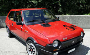 紅色經典Fiat 126p，帶有蠍子貼紙，停在石牆附近的碎石上。 — Steam Deck OLED 壁紙
