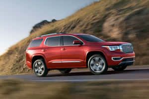 紅色GMC Acadia SUV在日落時分行駛在風景優美的山路上。 — 3:2 壁紙