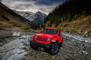 紅色Jeep Rubicon穿越岩石山間溪流，背景有白雪覆蓋的山峰。 — 汽車 4K 壁紙