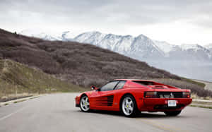 紅色法拉利 Testarossa 在山路上，背景有白雪覆蓋的山峰。 — 1280x800 壁紙