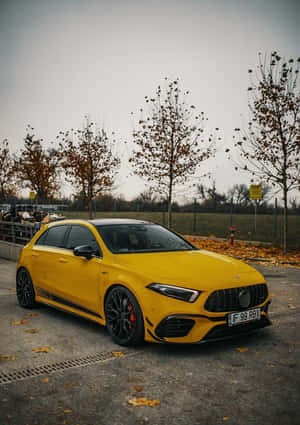 黃色 Mercedes-AMG A45 S 停泊在行人路上，背景有落葉和光禿的樹木。 — 酷車 壁紙