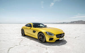 黃色 Mercedes-AMG GT S 在廣闊的鹽灘上，遠方有山巒。 — 黃色 壁紙