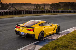 黃色Corvette停泊在日落時分的賽車場上，帶有輪胎護欄和橙色天空。 — Surface Laptop 壁紙