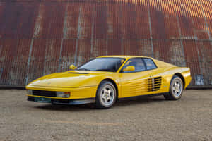 黃色法拉利 Testarossa 停在碎石地上，前面是生鏽的金屬牆，日落時分。 — Surface Pro 壁紙