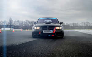 黑色BMW M3賽車在陰天下濕賽道上的橙色錐筒旁。