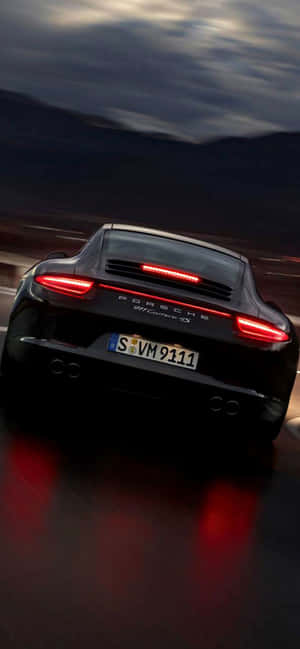 黑色保時捷911 Carrera 4S在黃昏時加速，紅色尾燈在潮濕路面上反射。 — iPhone 17e 壁紙
