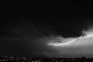 閃電在夜間城市上空閃爍，伴隨著黑暗的暴風雲。 — 雷暴 壁紙