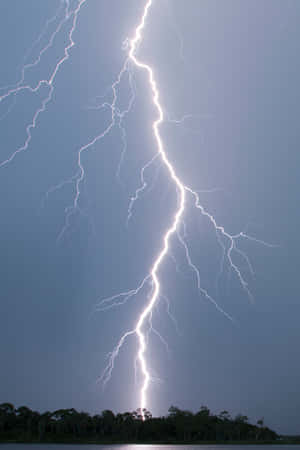 一道強烈的閃電照亮了湖泊和森林上空的暴風雨天空。