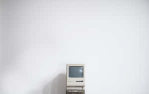 復古米色 Apple Macintosh 電腦放在木製支架上，背景是白色牆壁。 — 極簡美學 壁紙