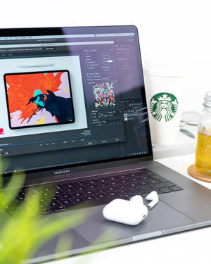 MacBook Pro 打開數位藝術，旁邊放著咖啡和耳塞，在乾淨的桌子上。 — 美學筆電 壁紙